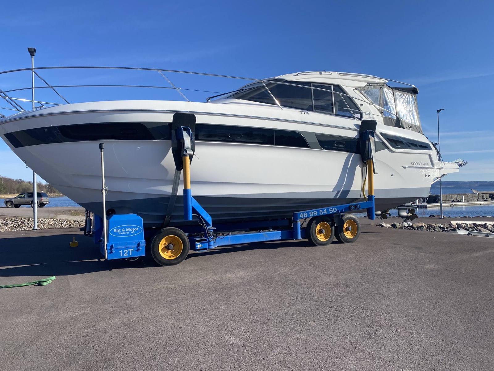 Hvit Bavaria Sport 400 på en blå hydraulisk båthenger fra Båt & Motorsenteret, med fjorden bak