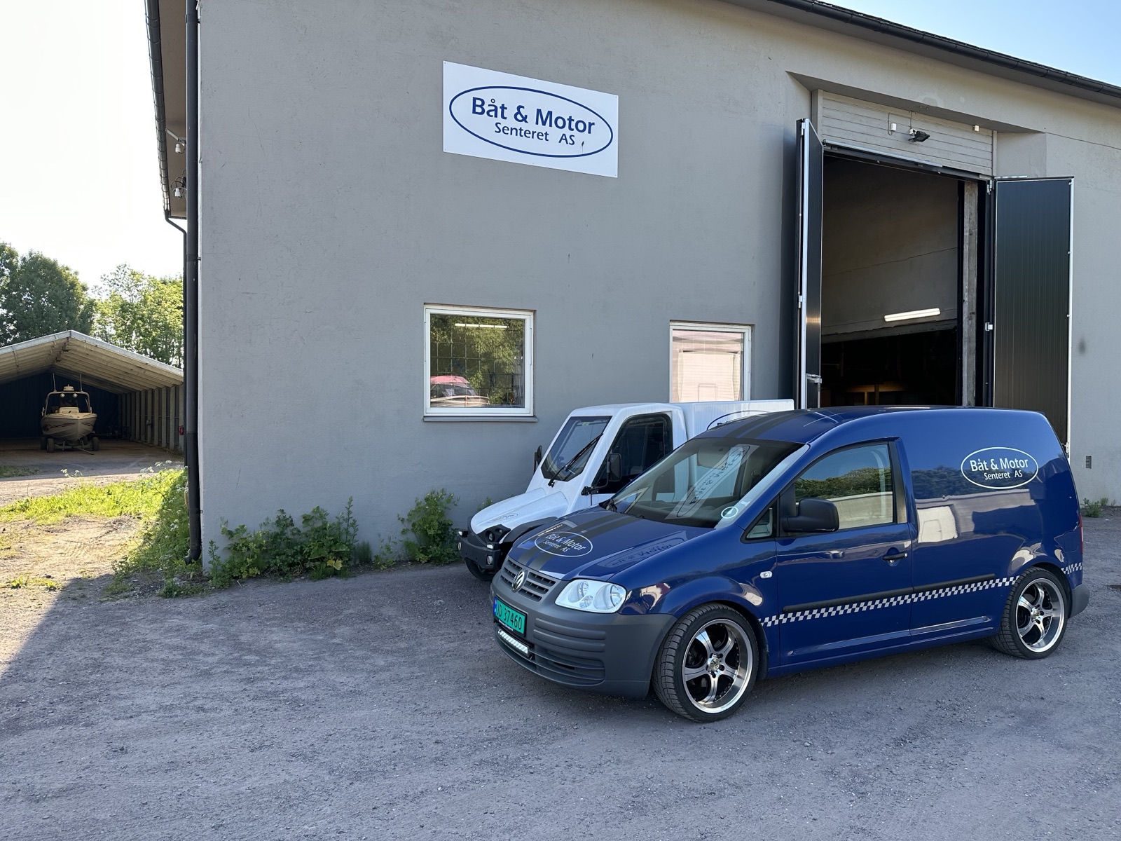 Verkstedbygget på Langgrunn med skiltet Båt & Motor Senteret AS og firmabilen foran åpen port
